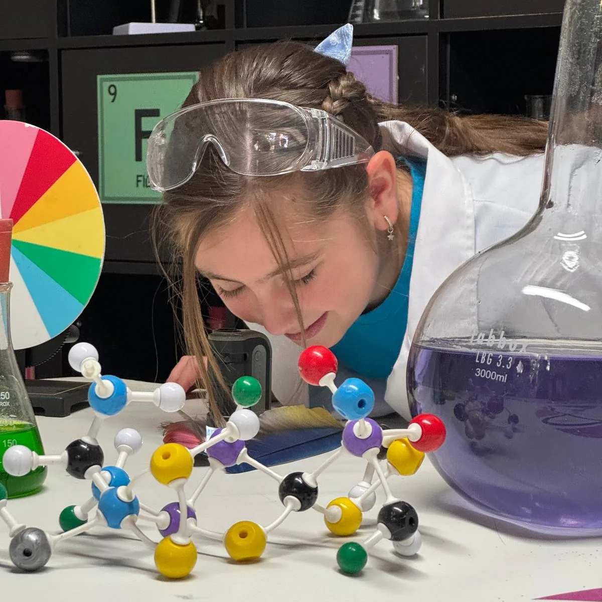 Niña con gafas de protección observando material de laboratorio en un taller de ciencia.